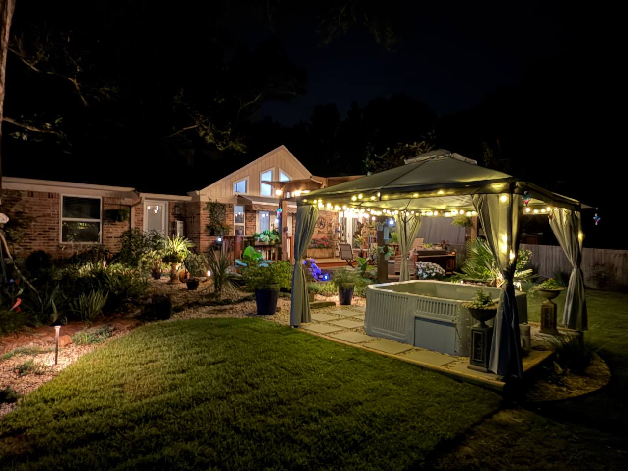 Wide view of the brick house and lit gazebo across an open lawn at night
