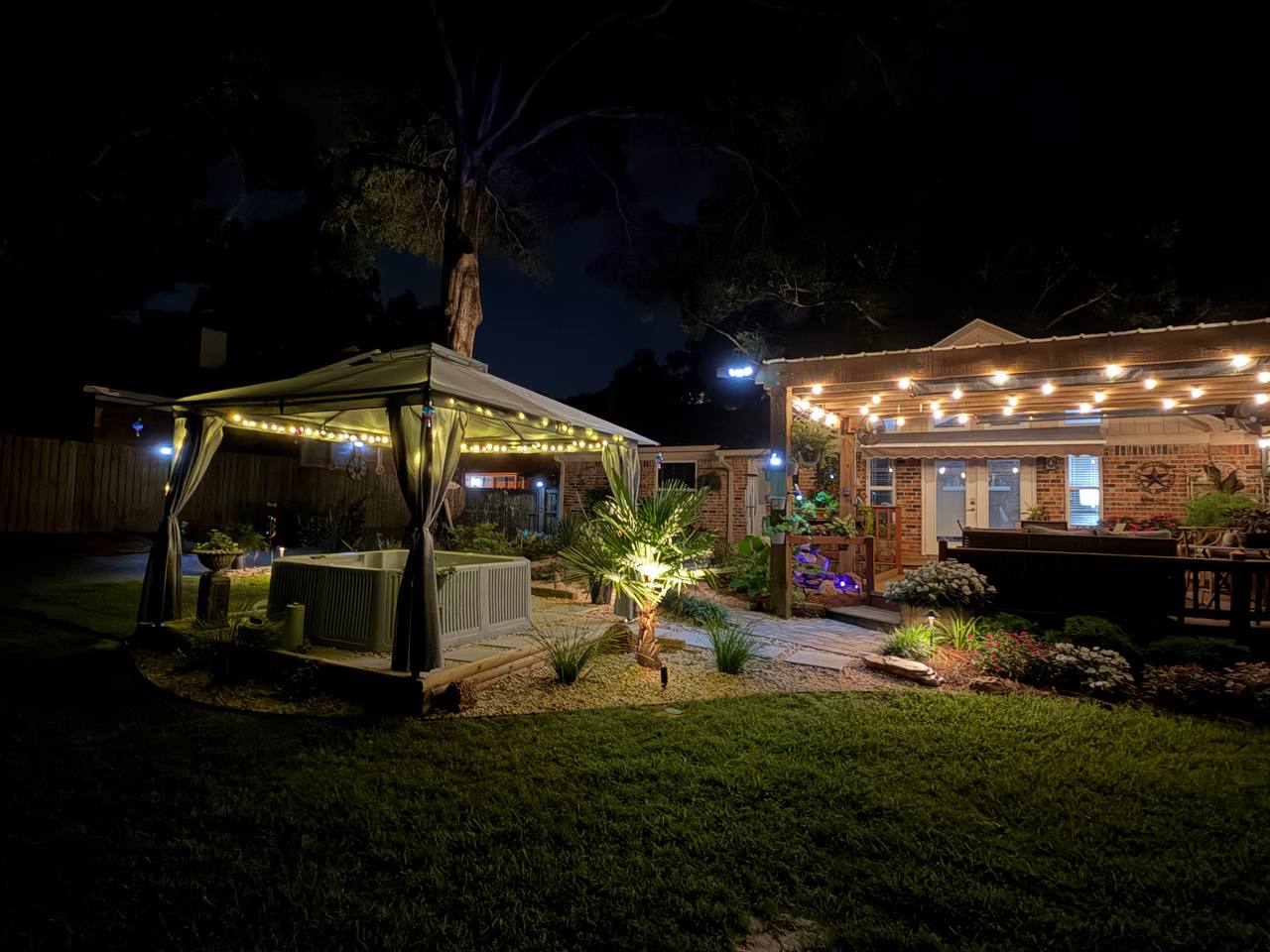 The gazebo at left and a string-lit covered patio at right, joined across a dark lawn
