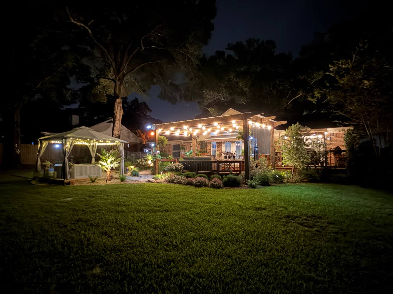 Distant view across the lawn showing the gazebo and string-lit patio glowing together