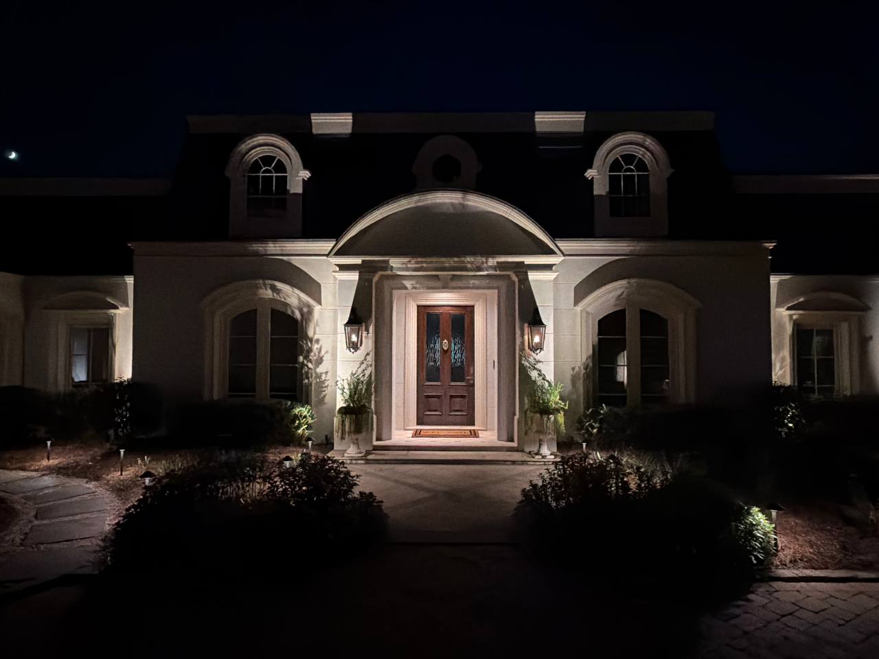 Symmetrical front entry with an arched portico, wall sconces flanking a wood door, and potted plants on either side